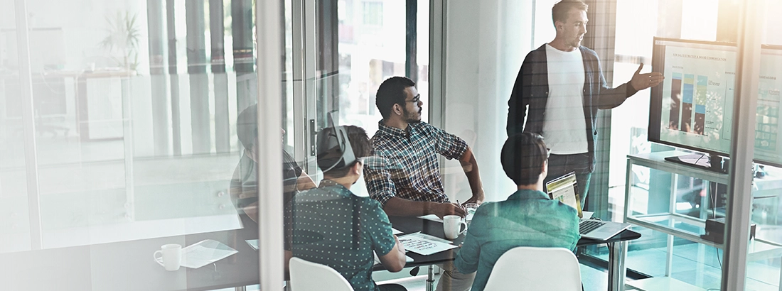 Team members in a glass-walled meeting room reviewing presentation slides during a business strategy discussion.